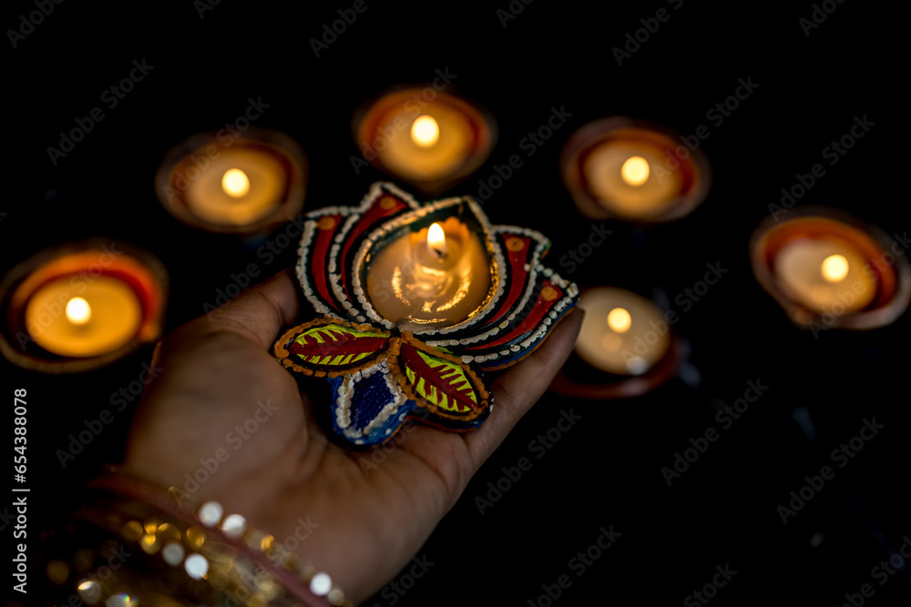 Happy Diwali - Woman hands with henna holding lit candle isolated on dark background.