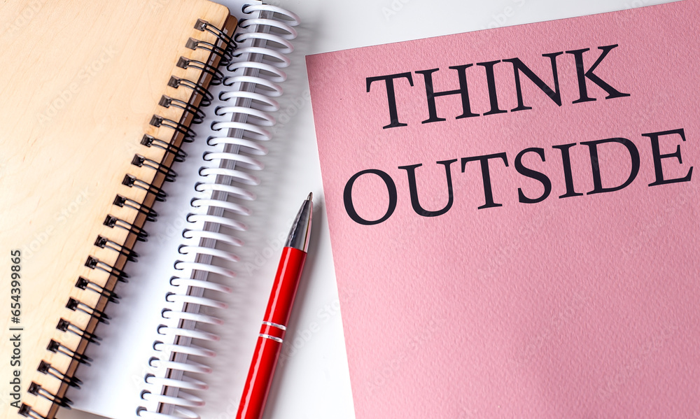 THINK OUTSIDE word on the pink paper with office tools on white background THINK OUTSIDE word on the pink paper with office tools on white background