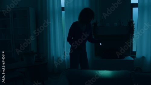 Woman girl lady female walking indoors in dark living room at night power war blackout electricity energy crisis outage searching lost things with flashlight at home without lights apartment darkness