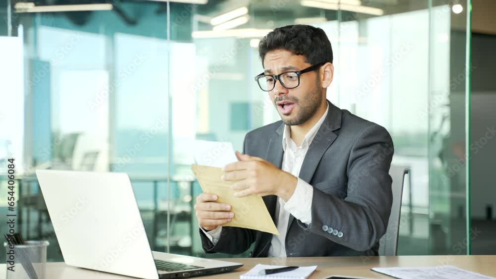 Disappointed young businessman in a formal suit reading a letter with bad news sitting at a workplace in a business office. Worried sad entrepreneur frustrated by received unpleasant notification Disappointed young businessman in a formal suit reading a letter with bad news sitting at a workplace in a business office. Worried sad entrepreneur frustrated by received unpleasant notification