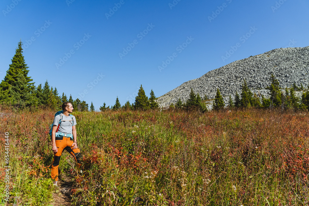 A hammered hipster with a backpack stands in the mountains, a guy looks at a stone peak, an autumn trip through the mountains, trekking alone.