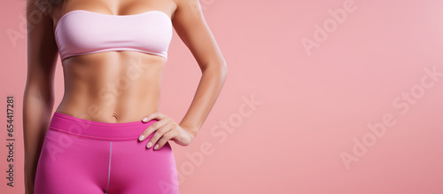 Cropped image of an athletic woman with beautiful flat belly isolated on pastel pink background with copy space. 