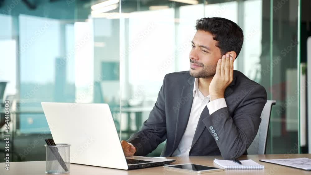 Earache. Sick young businessman in a formal suit suffers from ear pain sitting in office. Upset male touches his ear with his fingers. He has furuncle, shingles, eczema, ear diseases or otitis media Earache. Sick young businessman in a formal suit suffers from ear pain sitting in office. Upset male touches his ear with his fingers. He has furuncle, shingles, eczema, ear diseases or otitis media