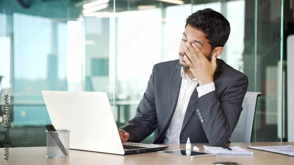 Overworked young businessman in a formal suit suffering from eye strain working on laptop sitting at workplace in office. Male instills eye medicine to improve vision recommended by an ophthalmologist Overworked young businessman in a formal suit suffering from eye strain working on laptop sitting at workplace in office. Male instills eye medicine to improve vision recommended by an ophthalmologist