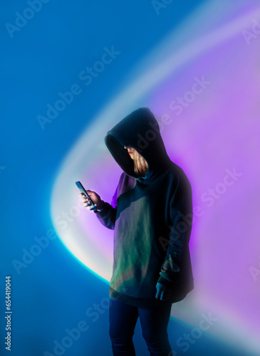 How to protect personal data and files on your phone. Unknown human in dark hoodie holding phone on neonlit backdrop.