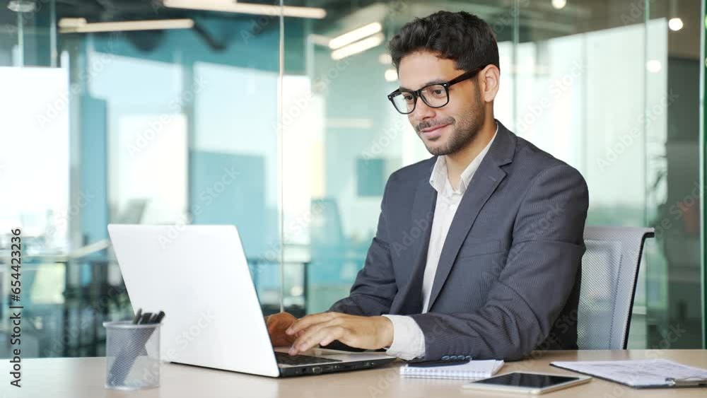 Young businessman in a formal suit typing on a laptop while sitting at a workplace in business office. Handsome entrepreneur working on a project on the computer, texting a client or chatting online