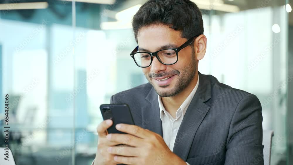Close up. Young businessman in formal suit is using smartphone while sitting at workplace in business office. Entrepreneur typing message, chatting, scrolling, browsing social media or shopping online