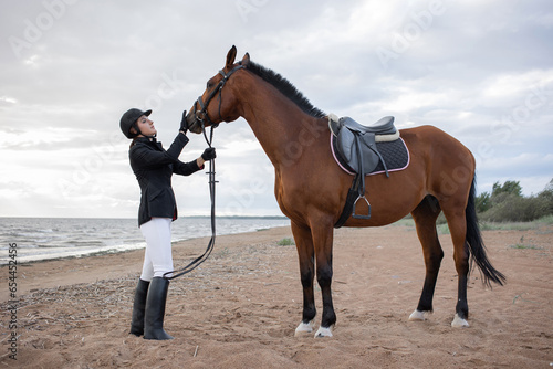 Equestrian sports. Horsewoman and her horse on the beach, portrait on the background of the sea, horseback riding outdoors