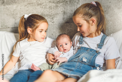 two sisters sit on bedroom with newborn son at home