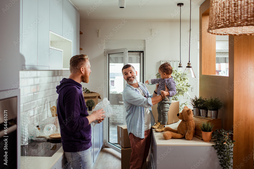 Young male gay couple playing with their son in the kitchen of their new apartment Young male gay couple playing with their son in the kitchen of their new apartment