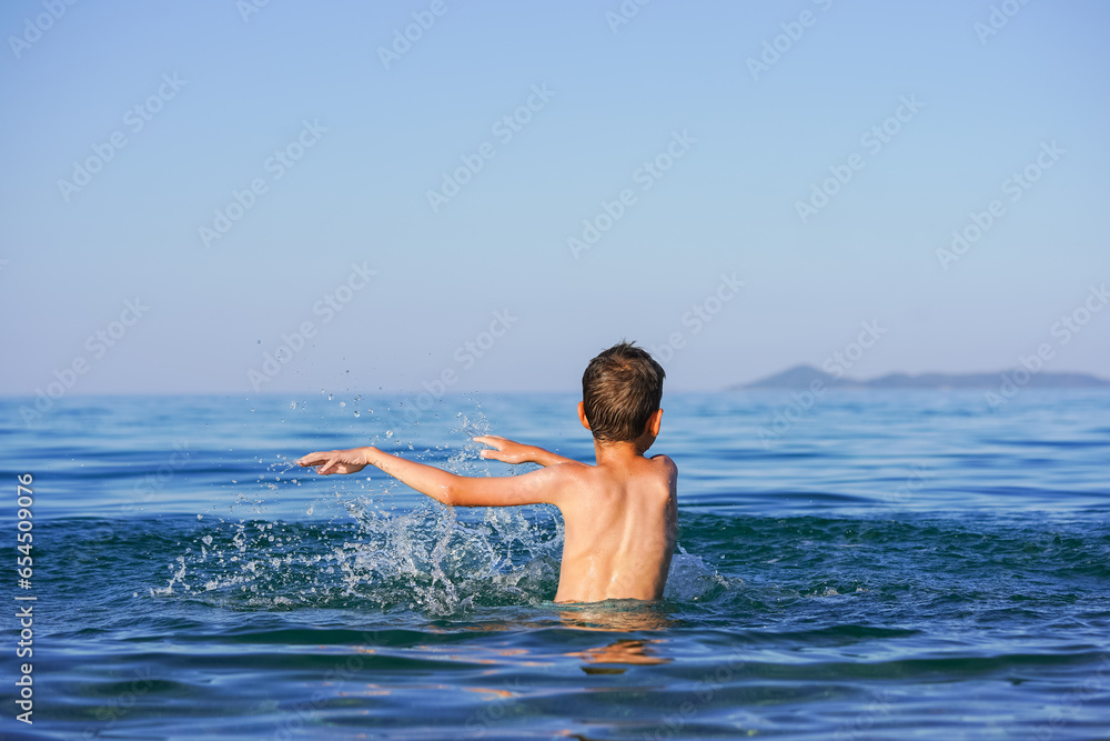 Blond Boy's Joyful Splash: End-of-Summer Fun on a Greek Beach with water flying around