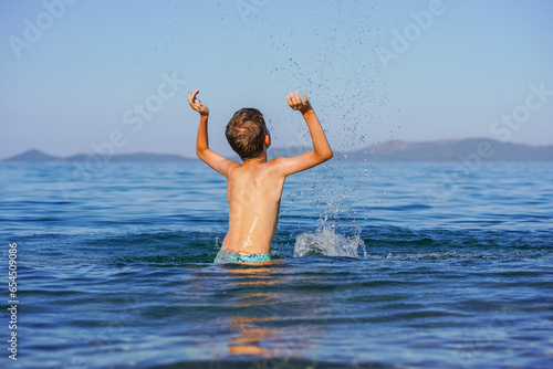 Blond Boy's Joyful Splash: End-of-Summer Fun on a Greek Beach with splashes upwards and water drop flying in the air