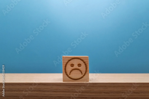 悪い印象の顔のマークのウッドキューブが中央にある机の上の青い背景