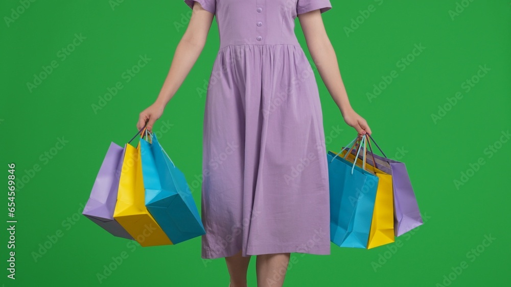 Colorful shopping bags in the hands of a walking woman. A woman with shopping bags walks in the studio on a green screen. Sale, Black Friday, discounts.