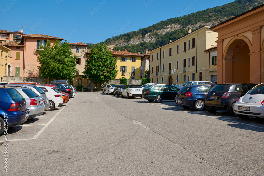 Cars parked in the outdoor parking places in modernized medieval Italian Canzo city, against Alp mountains background