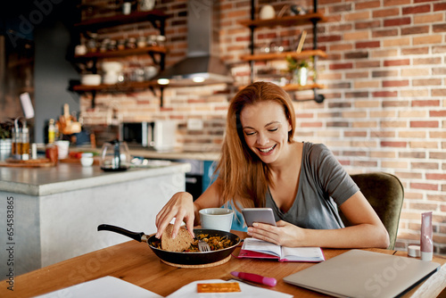 Young woman using the smartphone while having a healthy organic mean in the kitchen at home