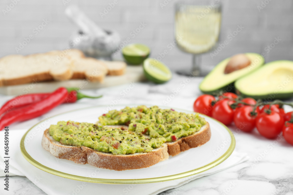 Delicious sandwiches with guacamole and ingredients on white table