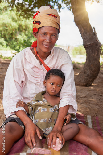 a happy bushmen San woman from Central Kalahari, holding her child, village New Xade in Botswana, in the yard of her home photo