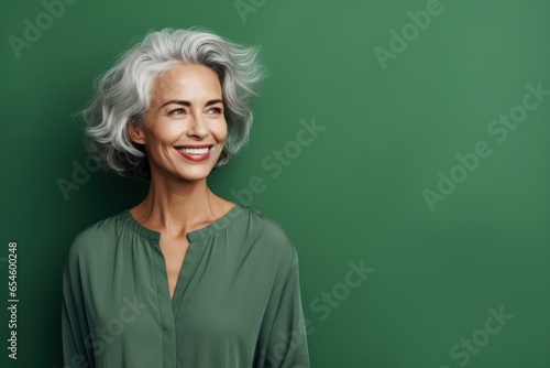 Joyful senior woman with grey hair, beaming at the camera. Vivid green backdrop accentuates her radiant spirit. Ideal for age-positive campaigns.