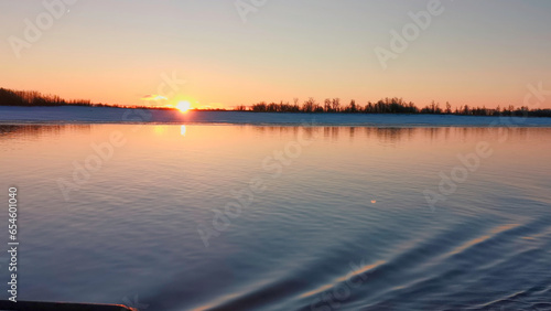 Beautiful sunset with sea surface and ripples from floating boat. Clip. Relaxing landscape with sea sunset and smooth water. Boat floats on sea surface near snowy shore and red sunset © Media Whale Stock