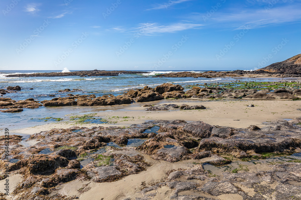 Tranquil beach seascape of the central Oregon Pacific coast with clear blue sky, clouds, stones and tidal pools. Tranquil beach seascape of the central Oregon Pacific coast with clear blue sky, clouds, stones and tidal pools.