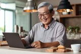 Generative AI : Smiling senior Asian man using mobile phone while working at home with laptop.