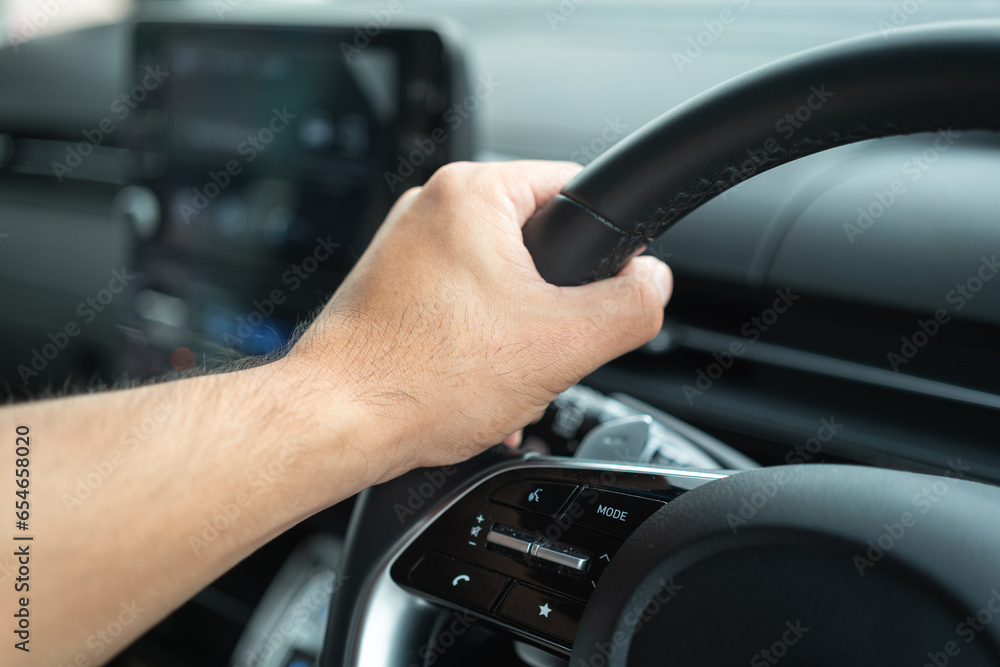 Action of a driver hand is handling on the multi-functional steering wheel during driving a car. Transportation in action photo, selective focus.