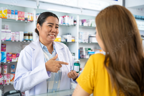 Pharmacist talking with customer at pharmacy counter. She tells customers about drug information at the pharmacy.