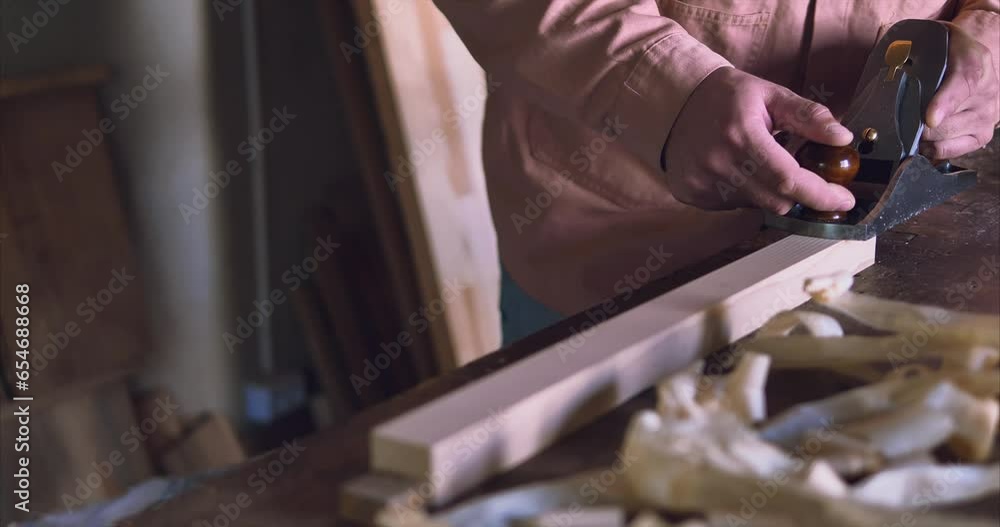 A carpenter in a long sleeve jacket works with a hand plane in a workshop with a workpiece. The video has high-quality sound A carpenter in a long sleeve jacket works with a hand plane in a workshop with a workpiece. The video has high-quality sound