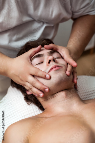 Top view of hands doctor therapist doing wellness face massage for sporty man  relaxing massaging head. Handsome athletic man visit masseur in medical room. Rehab massage concept. Copy ad text space