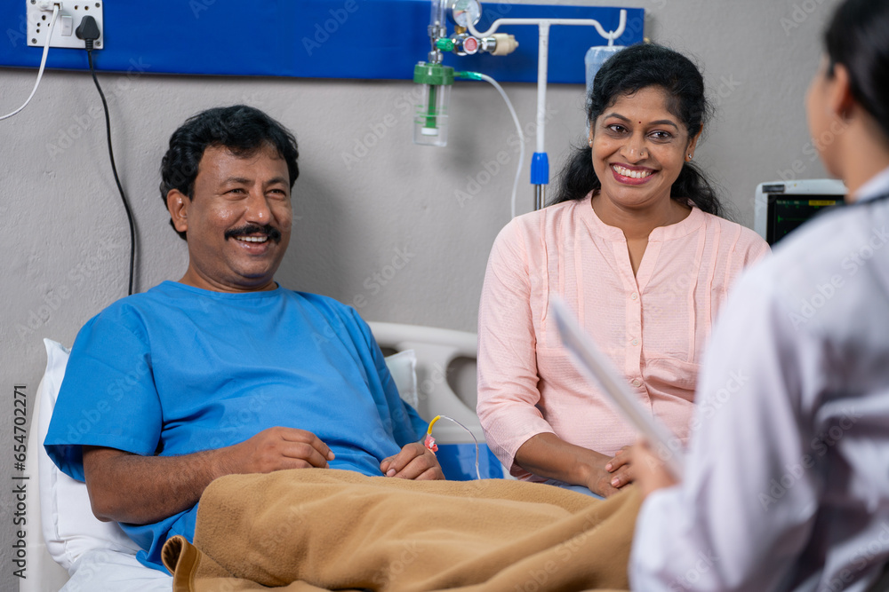 Obraz premium Shoulder shot of friendly indian doctor talking with recovered patient and wife at hospital - concept of successful treatment, medicare support and Conversation