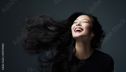 Smiling asian woman with wind in her black hair in studio