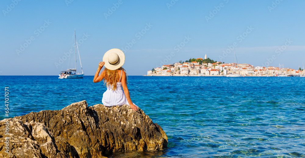 Φωτογραφία Young female tourist sitting on rock and looking at city in Croatia- Dalmatia- t