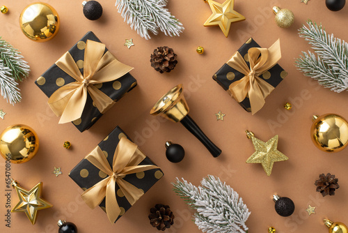 Get into festive mood with this Christmas scene. Top view of chic gift packages, black and gold balls, stars, delightful bell, frosted fir branches on terracotta backdrop, perfect or promotion