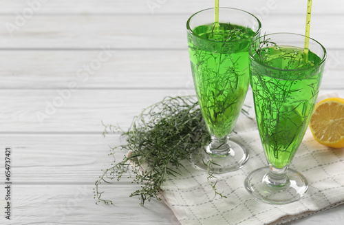 Glasses of homemade refreshing tarragon drink, sprigs and lemon on white wooden table, space for text photo