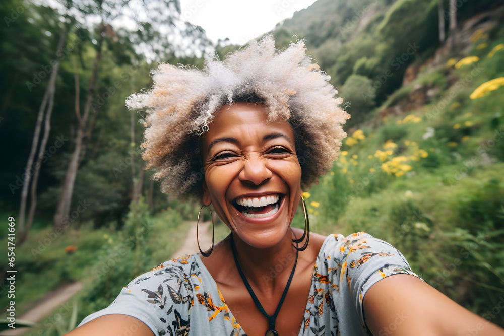 Smiling middle age black woman taking selfie while walking alone in mountains - obrazy, fototapety, plakaty 