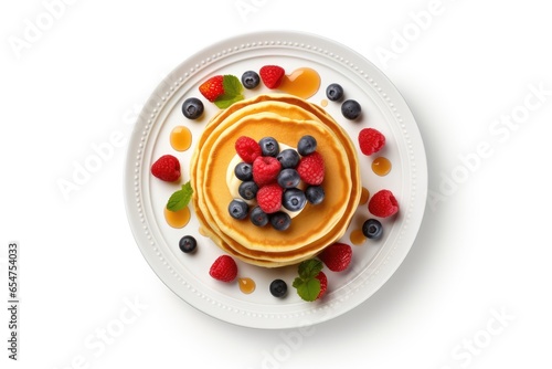 Top view of white plate with pancakes fresh berries and maple syrup