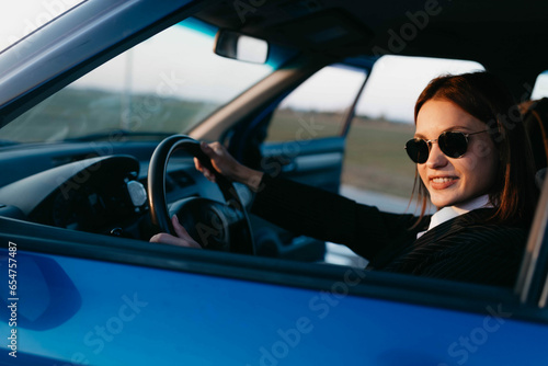 positive female driver in business clothes smiles while driving. Business driver work concept. © velimir