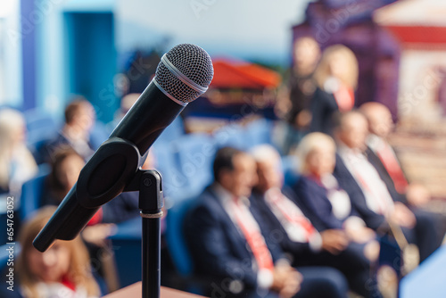 Microphone on podium. Blurred background of business people waiting for seminar, conference or speech.
