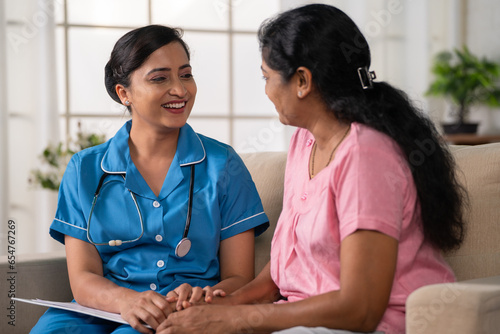 Side view shot of happy indian nurse with talking with recovered woman patient on sofa during home visit - concept of health care support, consultation and professional occupation
