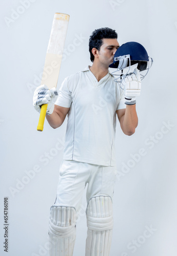 Indian man In cricket dress kissing helmet and showing his bat celebrating his century on isolated background , cricket concept photo