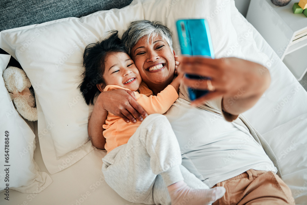 Selfie, smile and grandmother with child on bed bonding, relax and love for happy family with care. Photography, technology and senior woman with little girl in bedroom on video call together in home - obrazy, fototapety, plakaty 