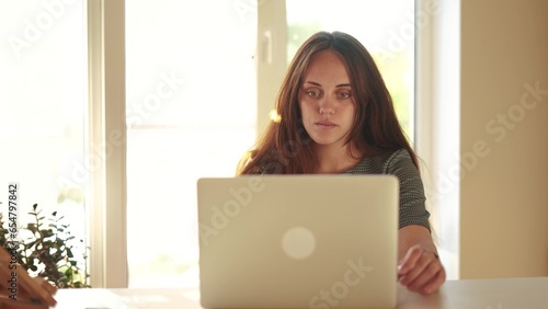 pretty girl working on a laptop at home near the window. learning students business work at home concept. girl student studying working on a laptop near the lifestyle window indoors in the classroom