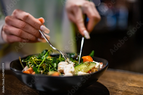 Woman's hands eat salad on table in restaurant