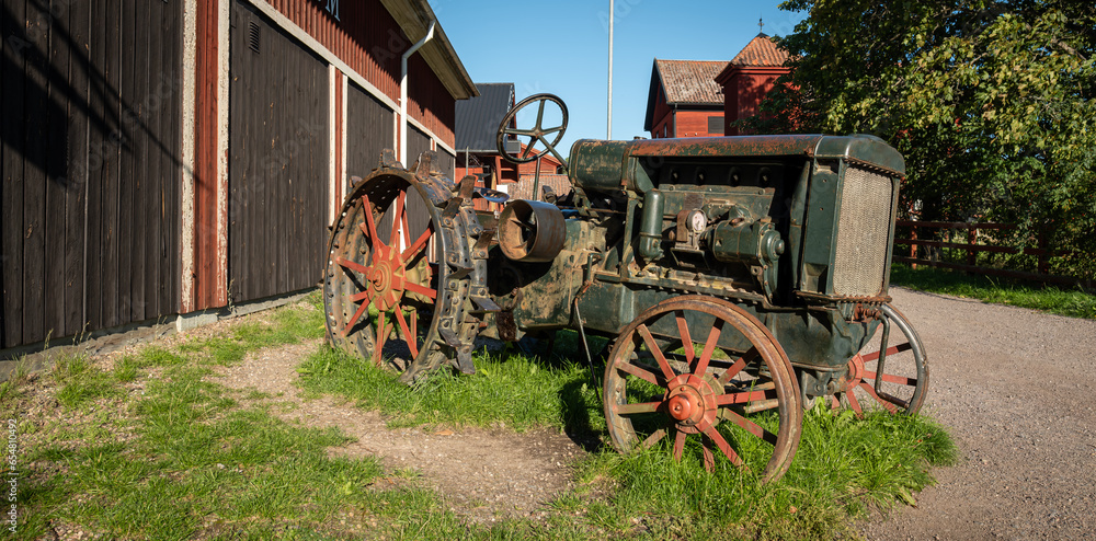 Old farm tractor besides a farm building during a warm summer afternoon