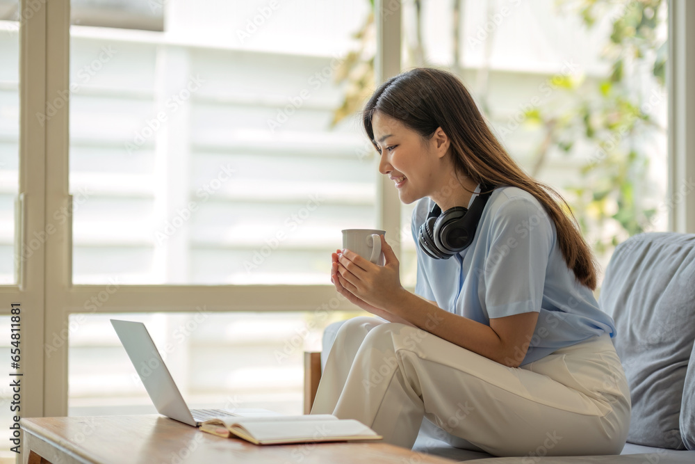 Fototapeta premium girl wearing headphones watching movies listening to music on laptop on the sofa at home on vacation with a cup of coffee
