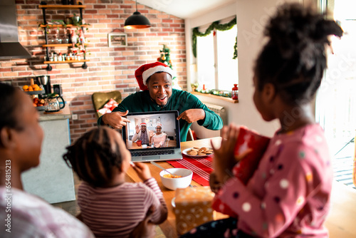 Young African American father surprises his children with a video call of their grandparents on a laptop at their home decorated for the Christmas and new year holidays photo