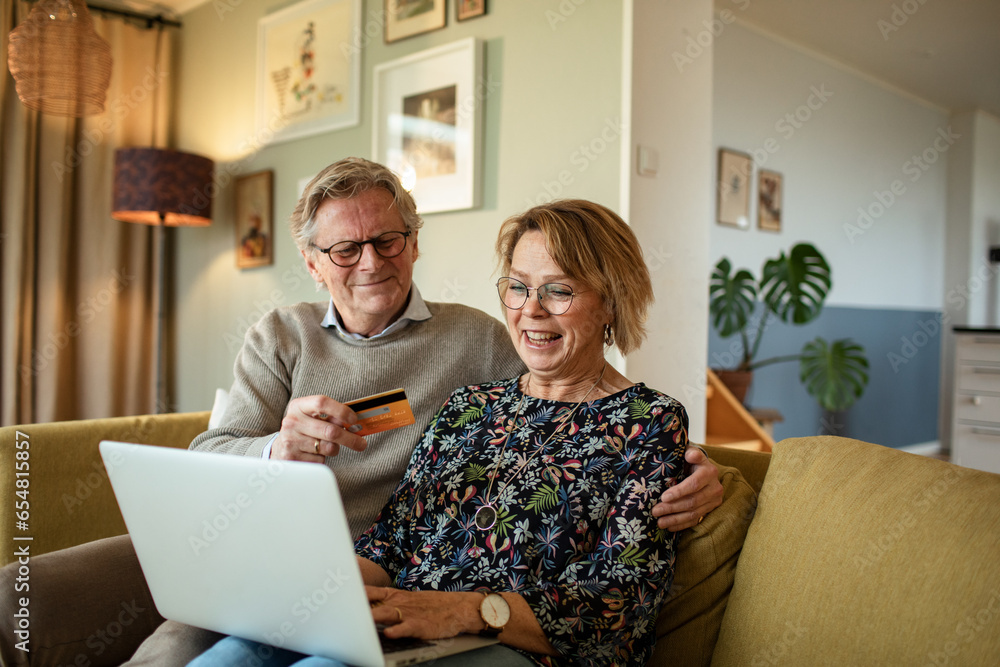 Senior Caucasian couple online shopping on the laptop on the couch at home Senior Caucasian couple online shopping on the laptop on the couch at home