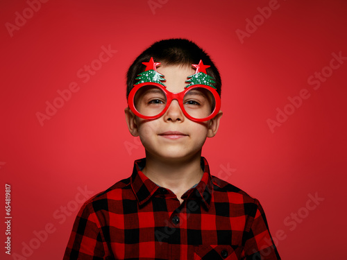 Little adorable boy in beautiful Christmas glasses against red background © Olena Shvets