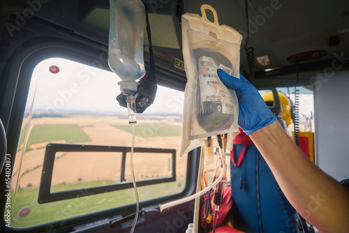 Hand of doctor holding transfusion bag with blood on board helicopter of emergency medical service during flight to hospital. Themes rescue, urgency and health care..